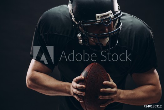 Picture of American football player with black helmet and armour running in motion holding ball getting ready to score a goal close up shot over dark background